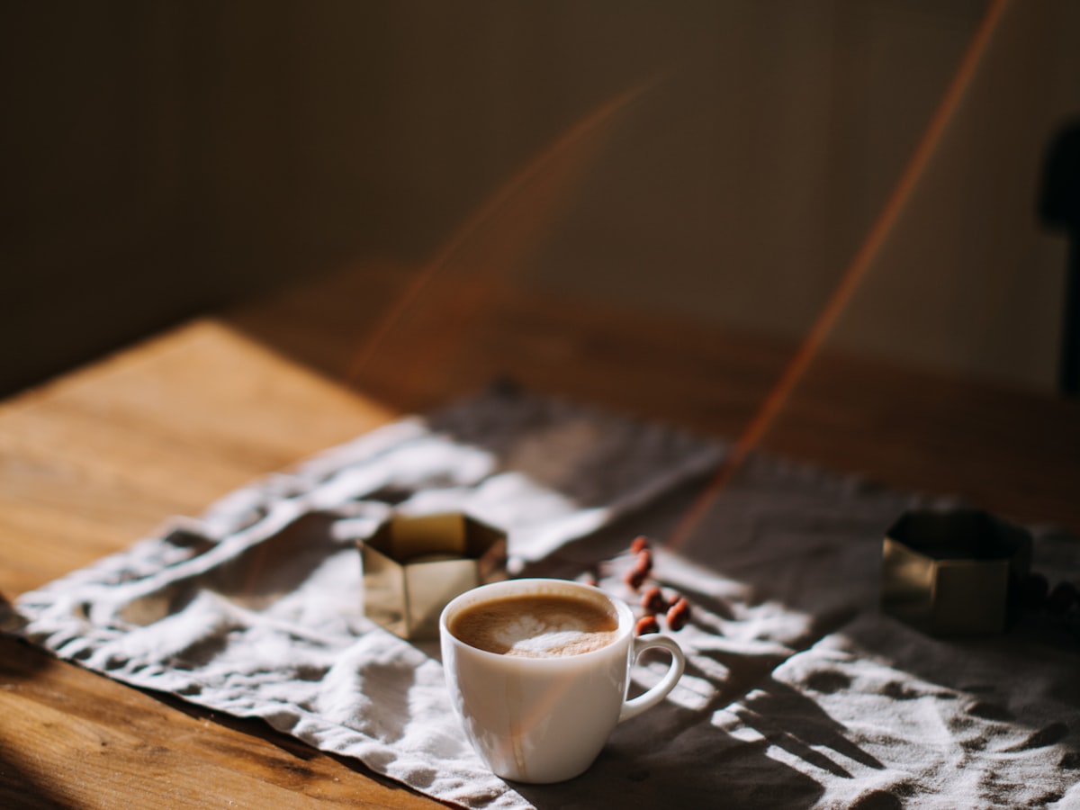 A cup of coffee on a linen cloth, lit by warm morning sunlight